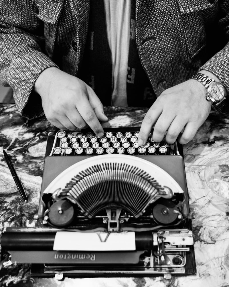 Paasha Motamedi's hands at the keys of a typewriter, a blank card in the platen